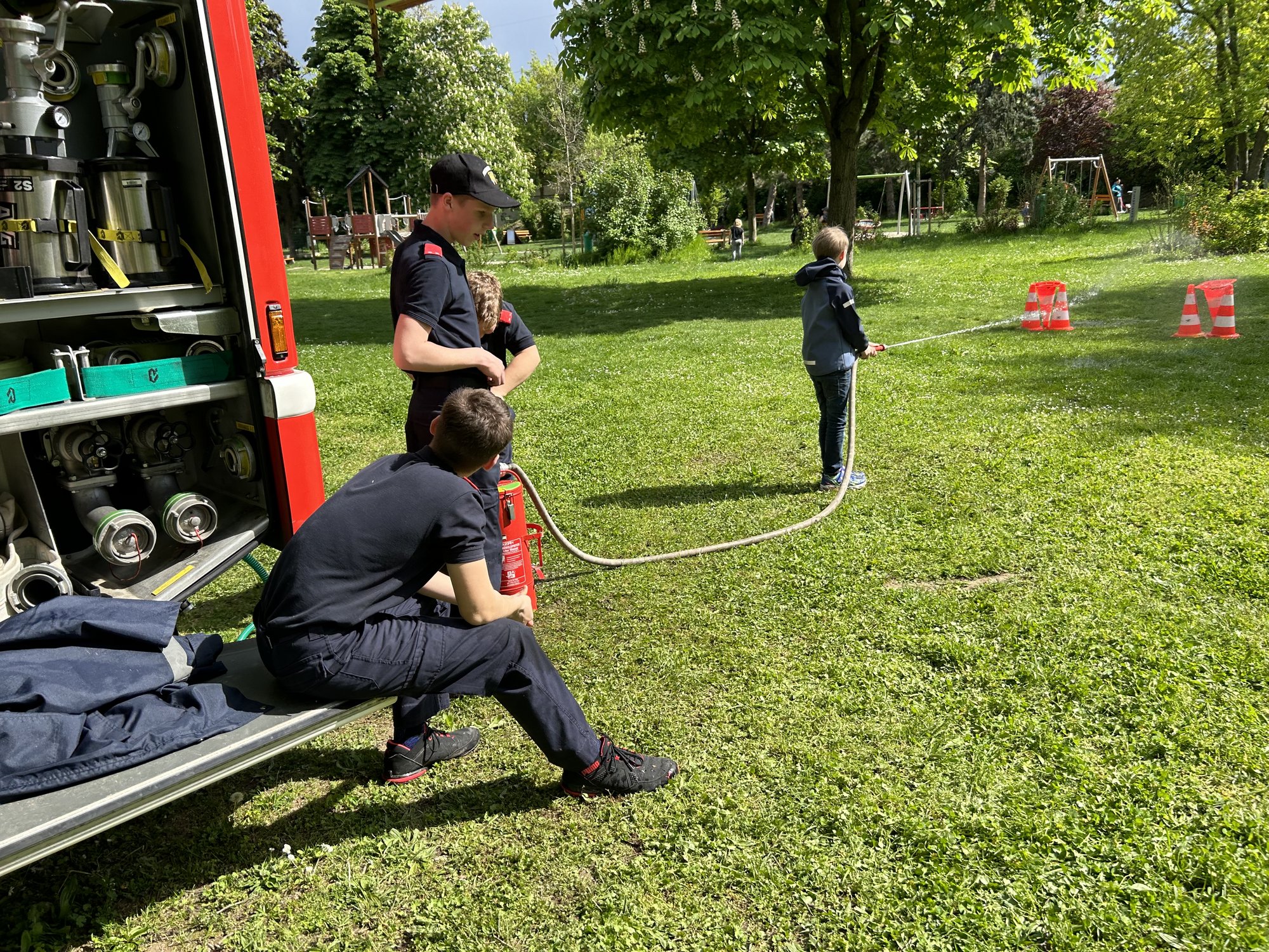 Mehrere Kinder sprühen Wasser mit dem Schlauch eines Feuerwehrautos